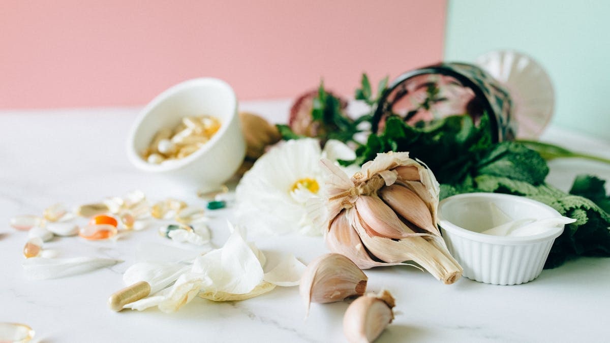 Flat lay of garlic, supplements, and herbs showcasing natural remedies on a marble surface.